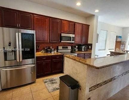 Fort Lauderdale, FL 33315 Kitchen featuring dark-toned cabinetry, stainless steel appliances, stone-finish countertops, a breakfast bar with a tile facade, and recessed ceiling lighting