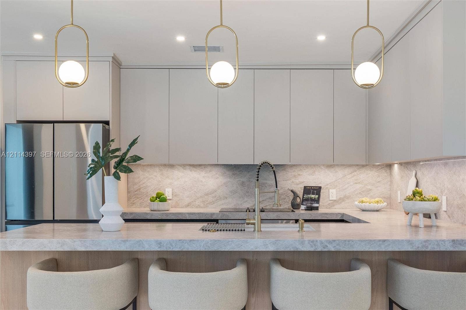14421 SW 85th Avenue, Palmetto Bay, FL 33158 Kitchen featuring custom flat-panel cabinetry, stone countertops with matching full-height backsplash, gold-tone hardware, and three pendant lights with spherical glass globes