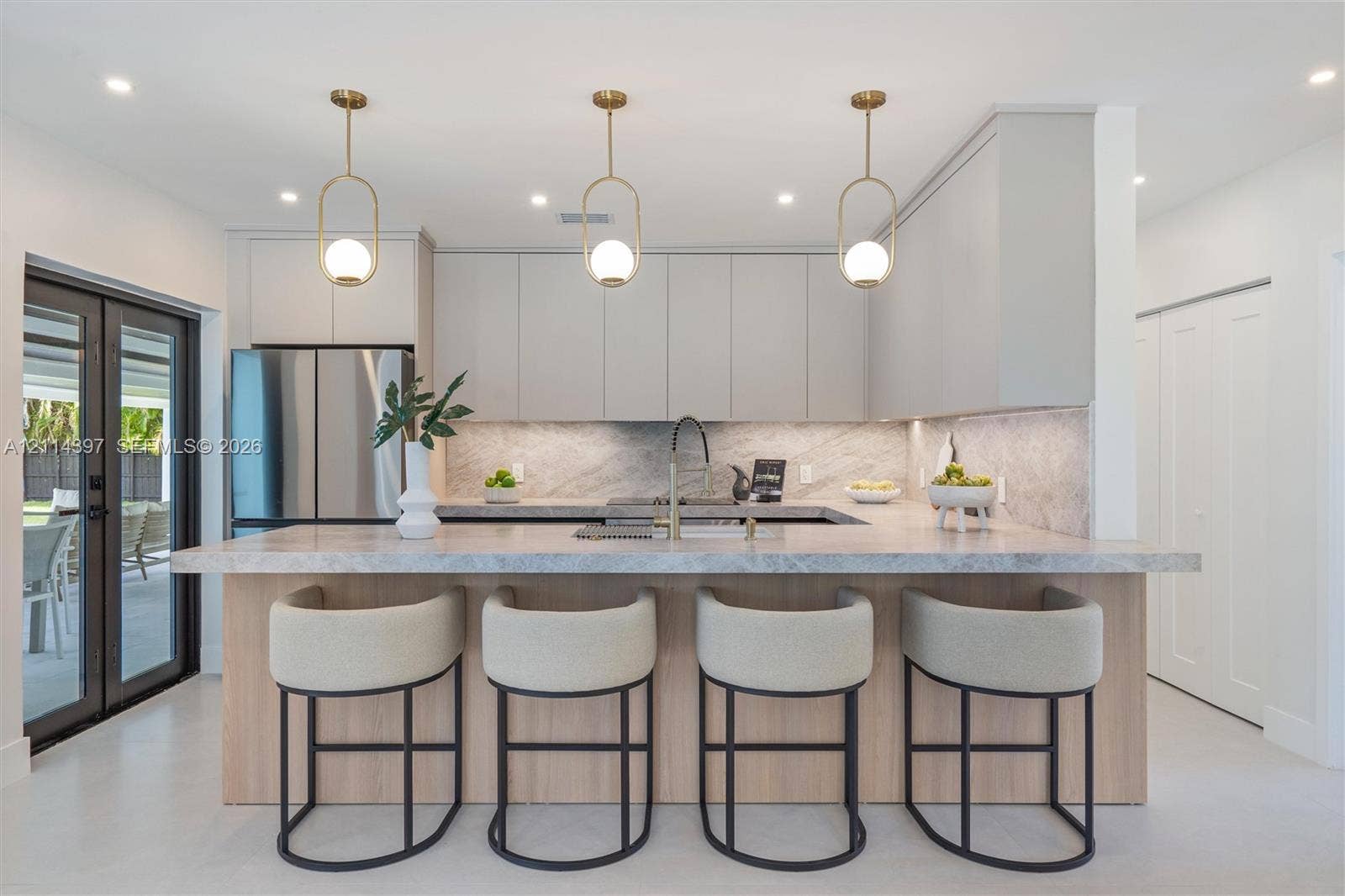 14421 SW 85th Avenue, Palmetto Bay, FL 33158 Kitchen featuring flat-panel cabinetry, a stone-surfaced kitchen island, three pendant light fixtures, stainless steel refrigerator, and a gooseneck faucet