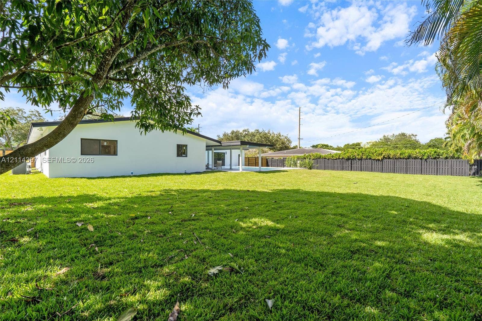 14421 SW 85th Avenue, Palmetto Bay, FL 33158 Expansive backyard featuring a large grass lawn, perimeter privacy fencing, mature trees, and a covered rear patio