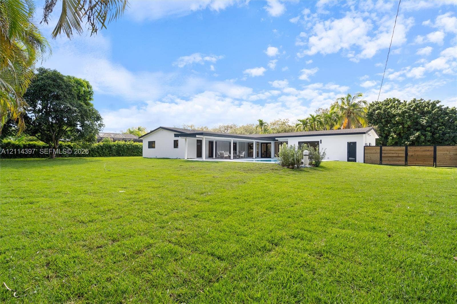 14421 SW 85th Avenue, Palmetto Bay, FL 33158 Expansive backyard featuring a sprawling lawn, mature trees, a horizontal-plank wood privacy fence, and a covered patio