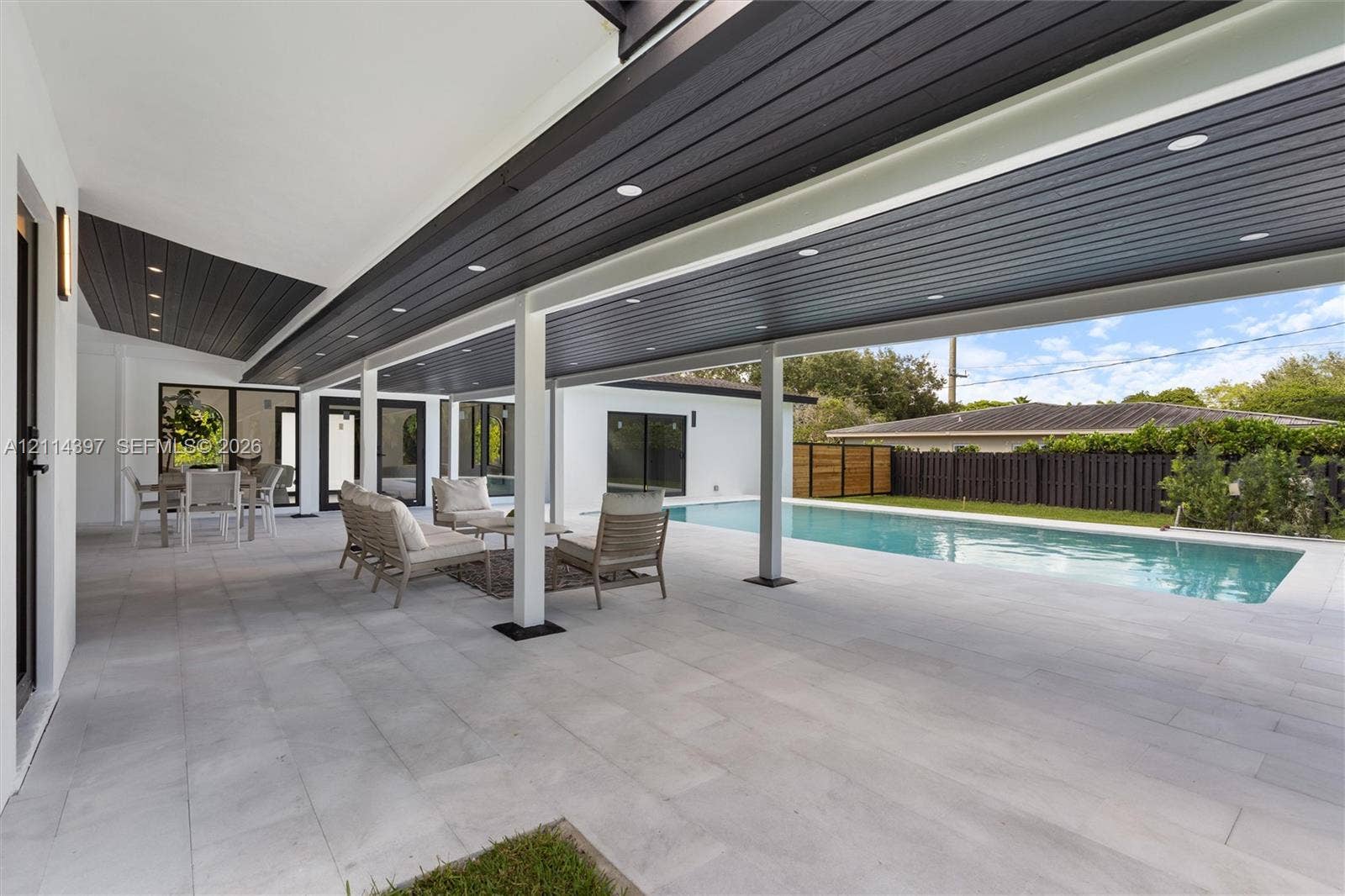 14421 SW 85th Avenue, Palmetto Bay, FL 33158 Covered outdoor patio featuring large-format tile flooring, recessed ceiling lighting, and a wood-finish ceiling, overlooking a rectangular swimming pool with integrated hardscaping
