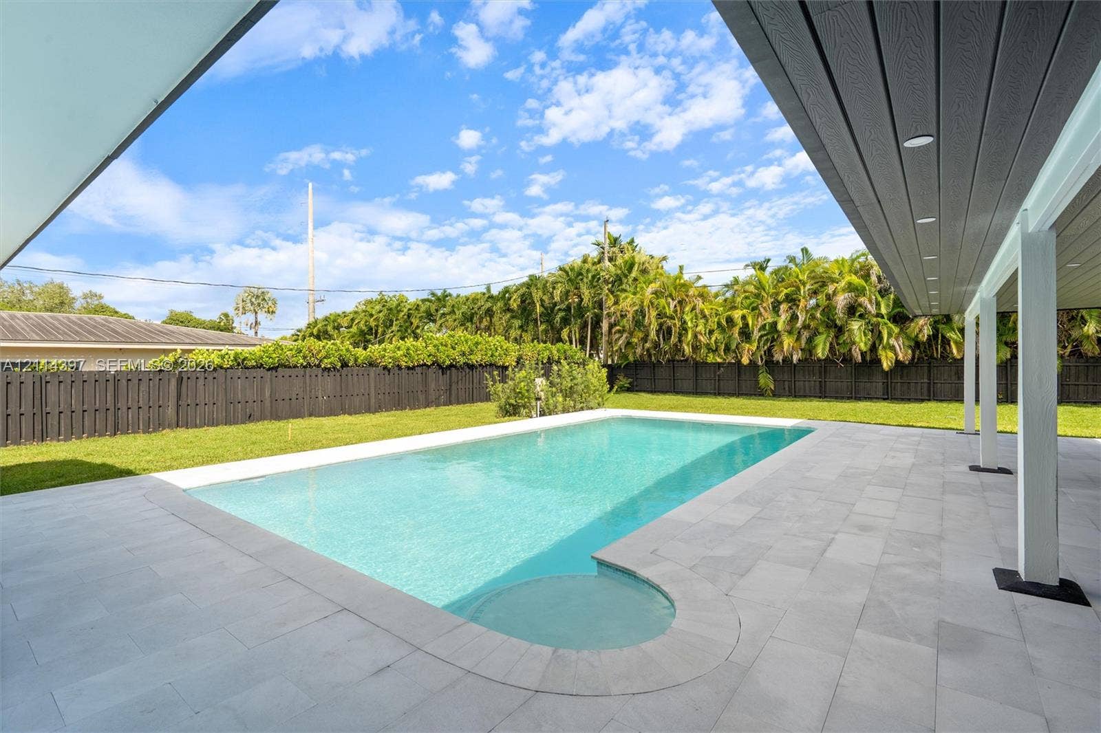 14421 SW 85th Avenue, Palmetto Bay, FL 33158 Rectangular in-ground pool featuring a tiled surround, covered patio area, and privacy fencing enclosing a lawn