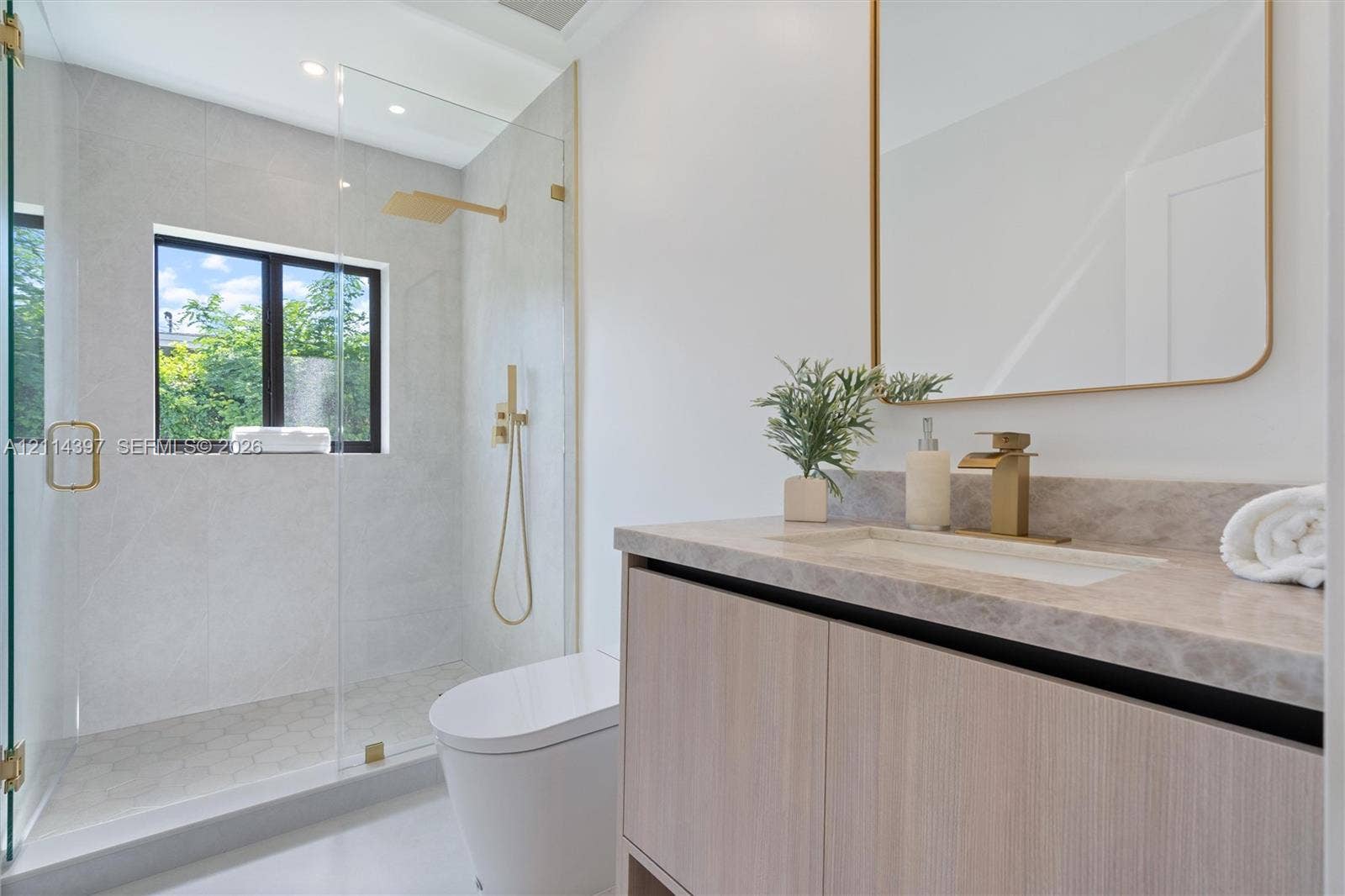 14421 SW 85th Avenue, Palmetto Bay, FL 33158 Modern vanity with stone-finish countertop, undermount sink, brass-tone hardware, wall-mounted mirror, and glass-enclosed walk-in shower with rainfall showerhead