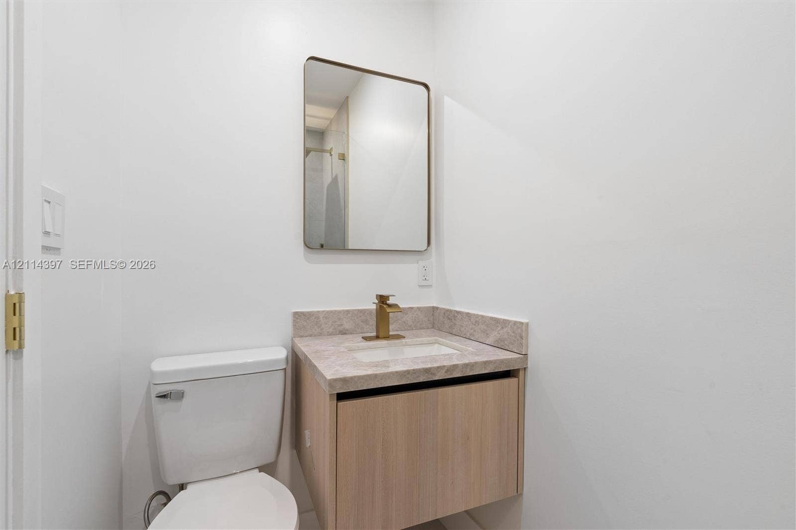 14421 SW 85th Avenue, Palmetto Bay, FL 33158 Floating vanity with a stone-finish countertop, undermount rectangular sink, brass-finish faucet, and rectangular wall-mounted mirror
