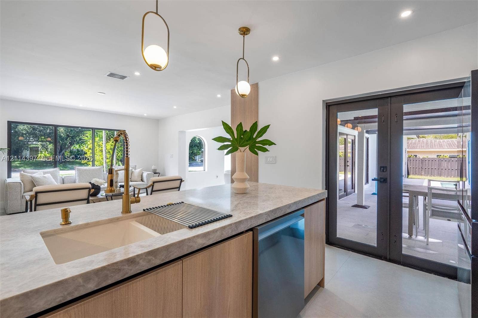 14421 SW 85th Avenue, Palmetto Bay, FL 33158 Kitchen island featuring stone-finish countertops, wood-finish cabinetry, an undermount sink with a brass-finish faucet, and modern pendant lighting