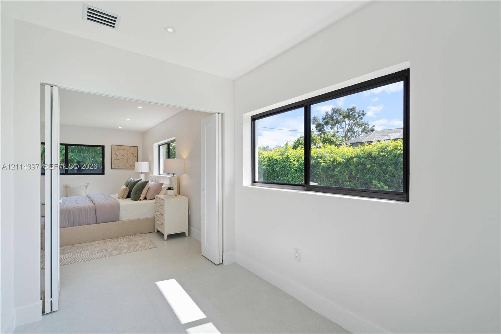 14421 SW 85th Avenue, Palmetto Bay, FL 33158 Interior space featuring light-toned flooring, neutral wall finishes, black-framed horizontal windows, and white bifold doors