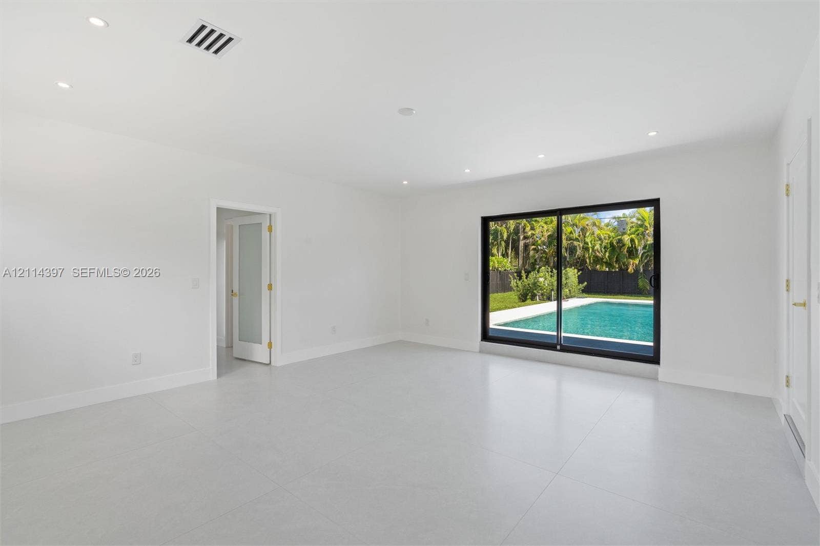 14421 SW 85th Avenue, Palmetto Bay, FL 33158 Open interior space featuring light-toned tile flooring, recessed ceiling lighting, a sliding glass door with a dark frame, and a frosted glass panel door