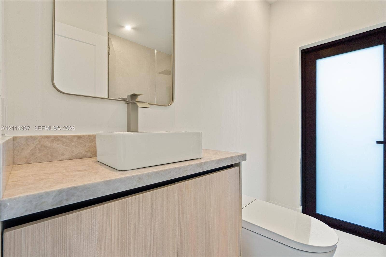 14421 SW 85th Avenue, Palmetto Bay, FL 33158 Wood-finish floating vanity with a stone countertop, rectangular vessel sink, polished metal faucet, and wall-mounted mirror