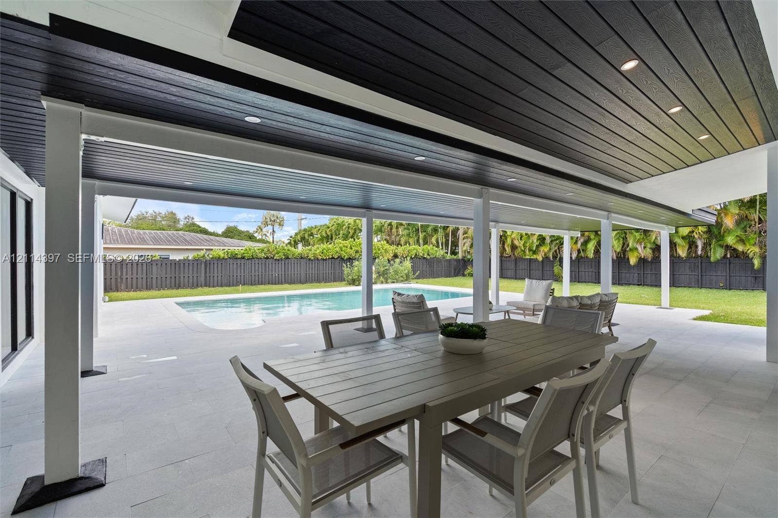14421 SW 85th Avenue, Palmetto Bay, FL 33158 Covered outdoor patio featuring a dark-stained wood tongue-and-groove ceiling, recessed lighting, white support pillars, light-toned paved flooring, and an in-ground swimming pool