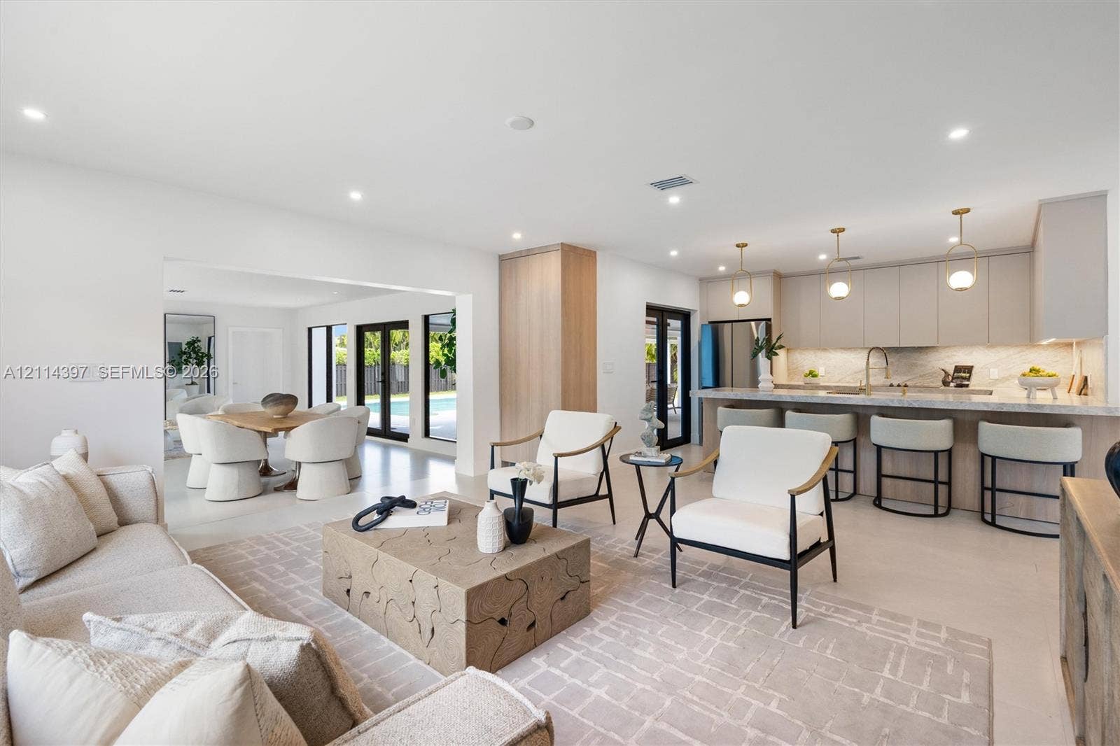 14421 SW 85th Avenue, Palmetto Bay, FL 33158 Open-concept interior featuring light-toned flooring, recessed lighting, a chef's kitchen with stone-surfaced countertops, custom flat-panel cabinetry, and multi-light pendant fixtures