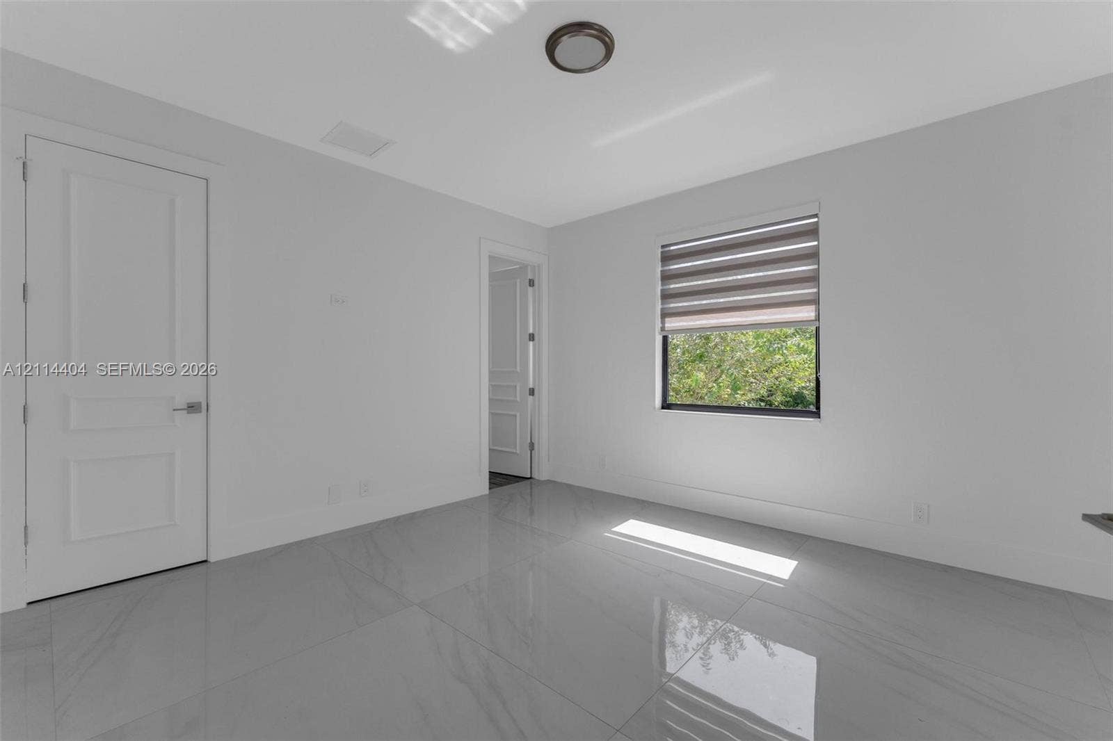 Interior room featuring large-format tile flooring, neutral walls, two paneled doors, and a window with integrated shade