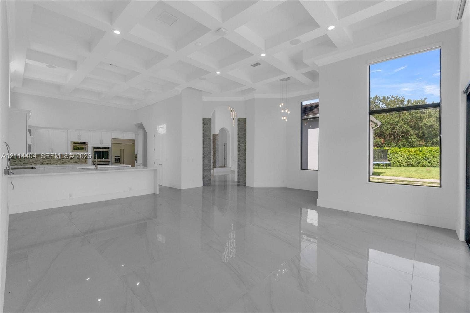 Coffered ceiling with recessed lighting, large-format tile flooring, quartz-surfaced kitchen island, built-in stainless steel appliances, and floor-to-ceiling windows