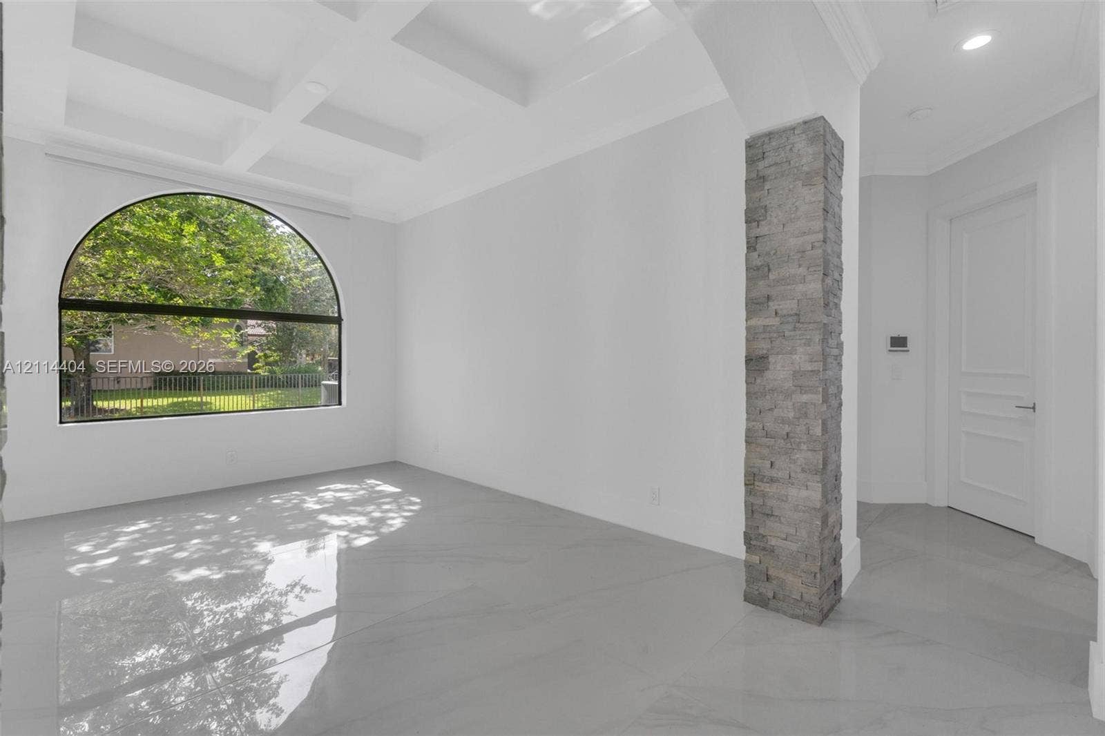Coffered ceilings, large arched window, polished stone-finish flooring, and a decorative stacked-stone column