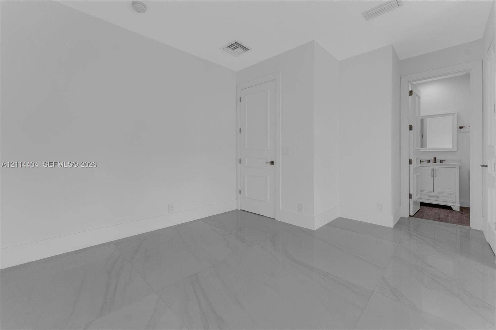 Neutral-toned room featuring large-format tile flooring, a multi-panel interior door, and smooth wall finishes