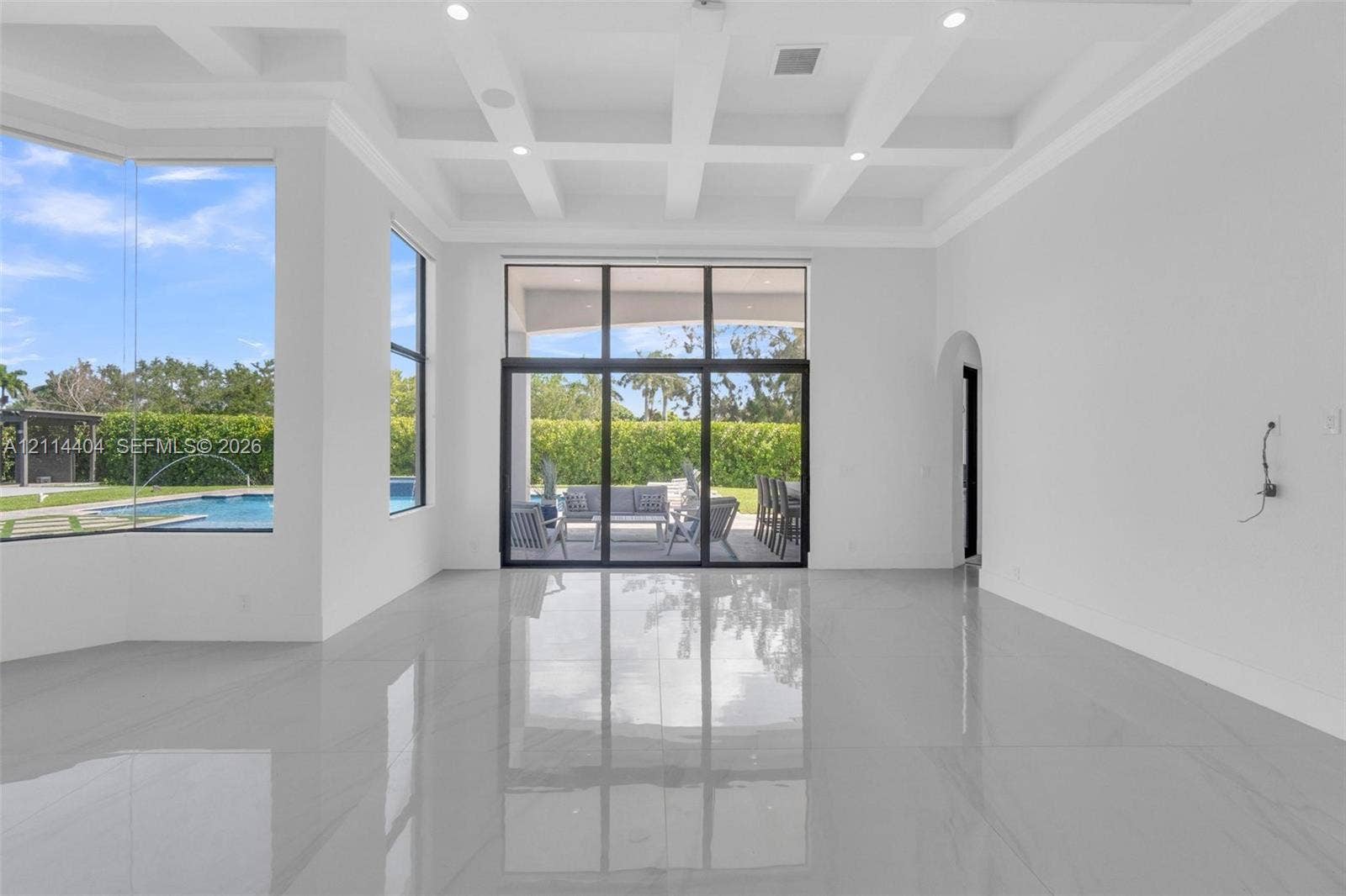 Coffered ceiling, expansive multi-panel floor-to-ceiling glass doors, large-format tile flooring, and oversized windows