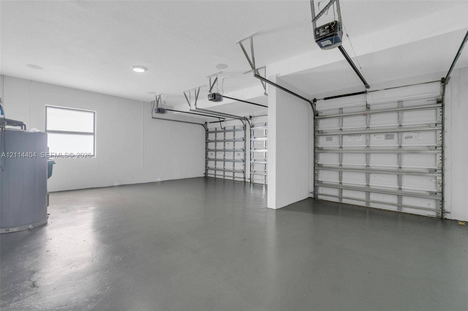 Three-car garage featuring a smooth-finished floor, white-painted walls, overhead garage door openers, and a dedicated window