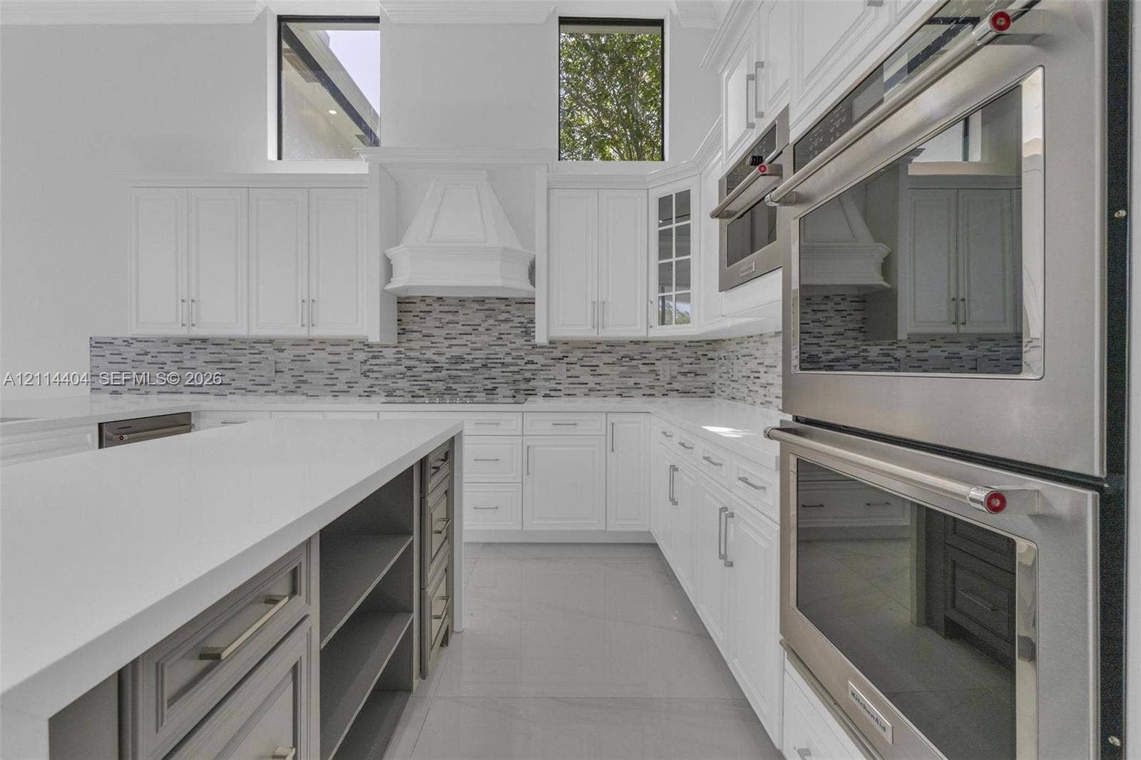 Kitchen featuring white cabinetry, quartz countertops, a stone tile backsplash, stainless steel double wall ovens, and a central island with built-in storage