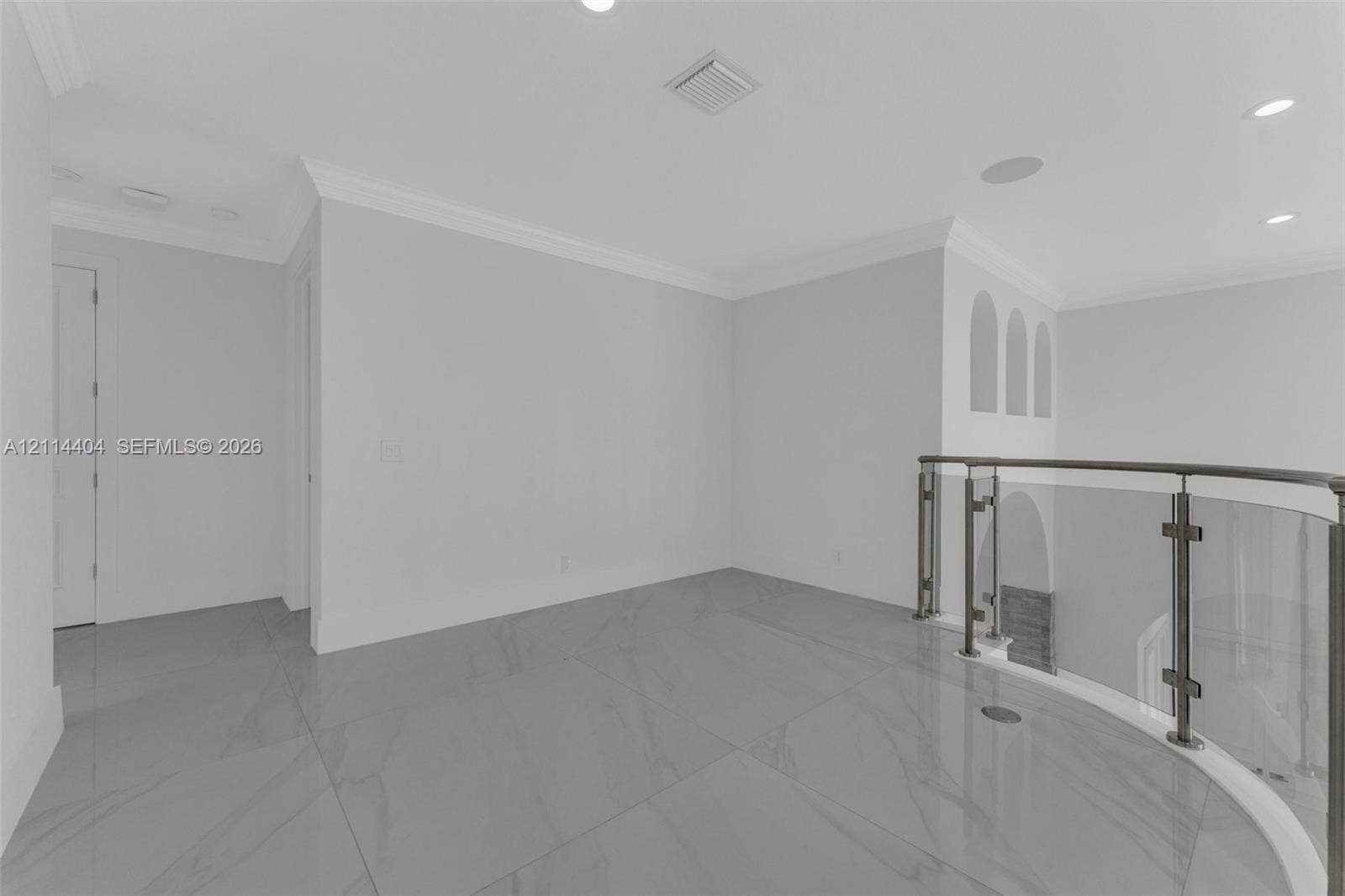 Large-format tile flooring, glass-panel railing with metal hardware, crown molding, recessed lighting, and arched wall niches