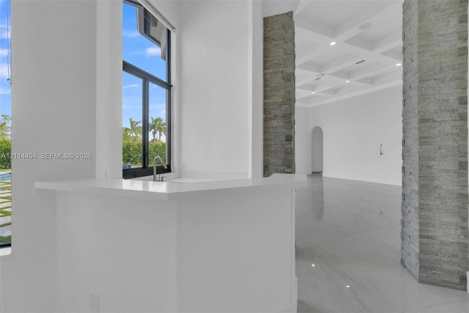 Interior space featuring coffered ceilings, stacked stone columns, porcelain-finish flooring, and a stone-topped bar with an integrated sink