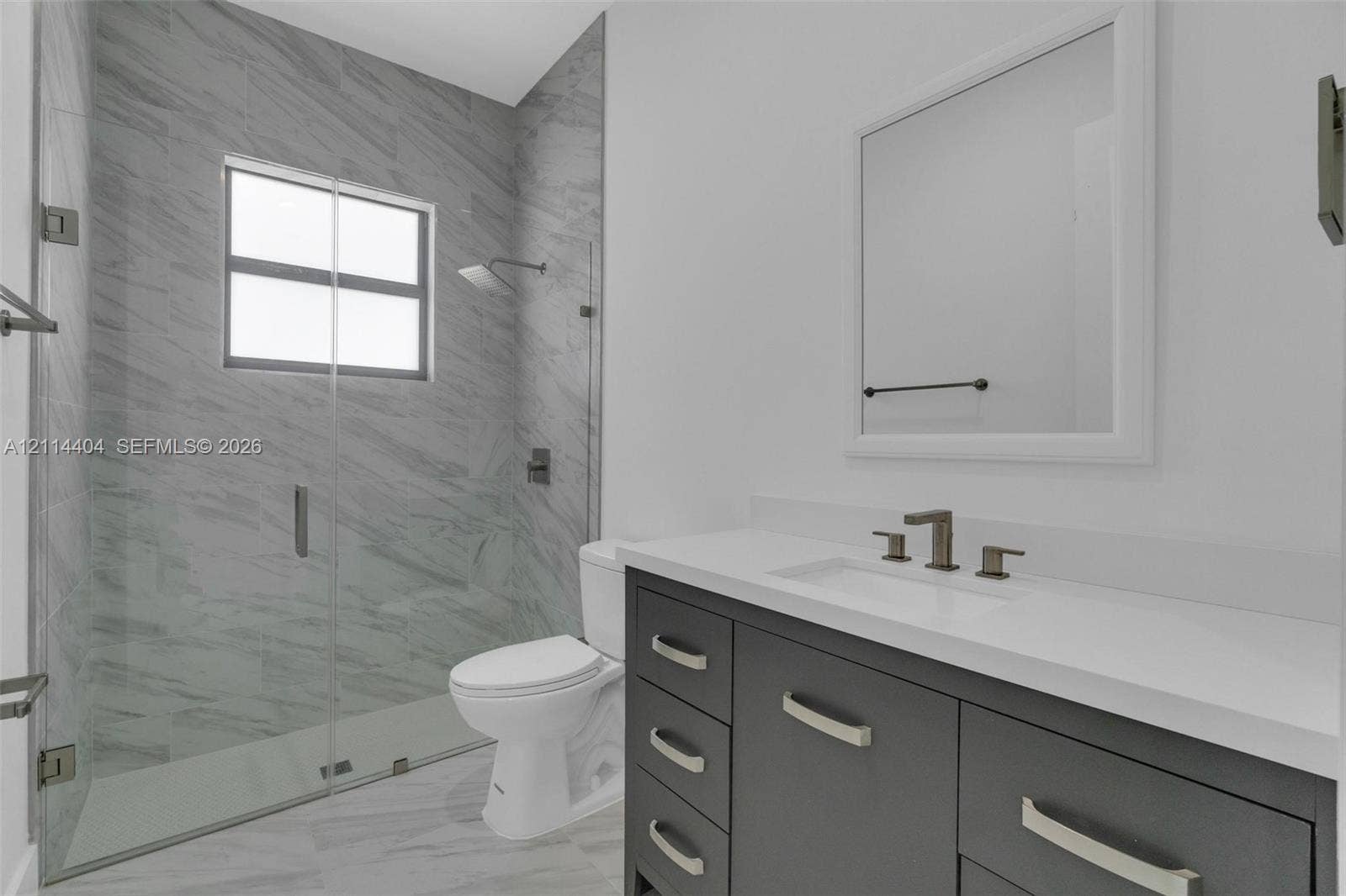 Bathroom featuring a dark gray vanity with a solid surface countertop, rectangular under-mount sink, walk-in shower with floor-to-ceiling tile, and a framed mirror