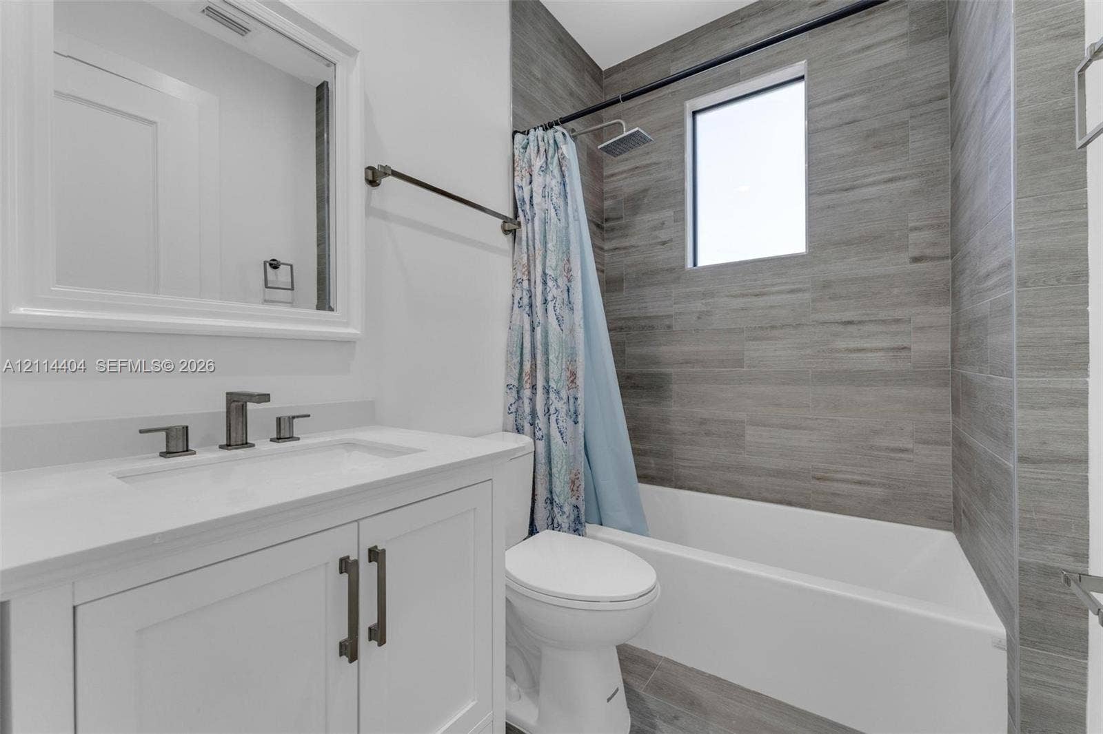 Bathroom featuring a white vanity cabinet with a stone countertop, a framed wall mirror, and a tub-shower combination enclosed by floor-to-ceiling textured tile wall cladding