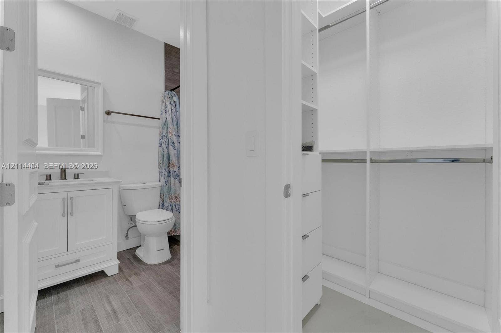 Bathroom featuring a white vanity cabinet with a light-toned countertop, wood-finish flooring, and a walk-in closet with integrated white shelving and hanging rods
