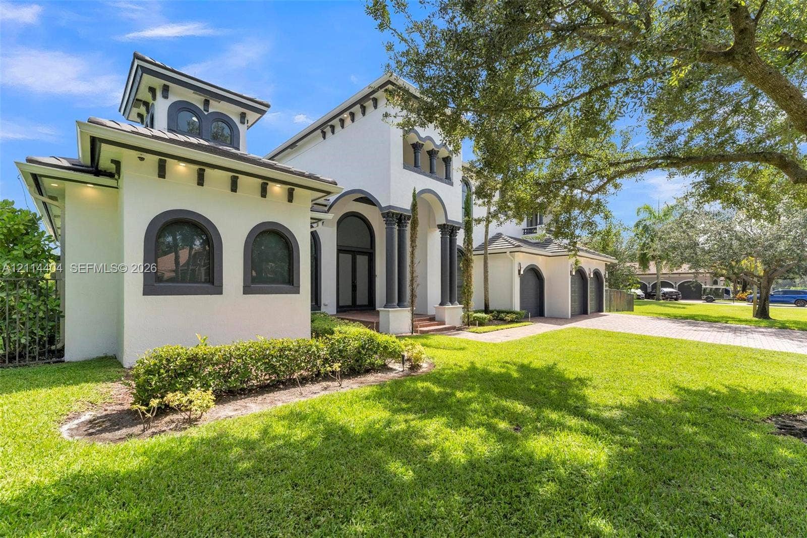Stucco exterior featuring arched windows, decorative corbels, multi-car garage, and columns at the entryway