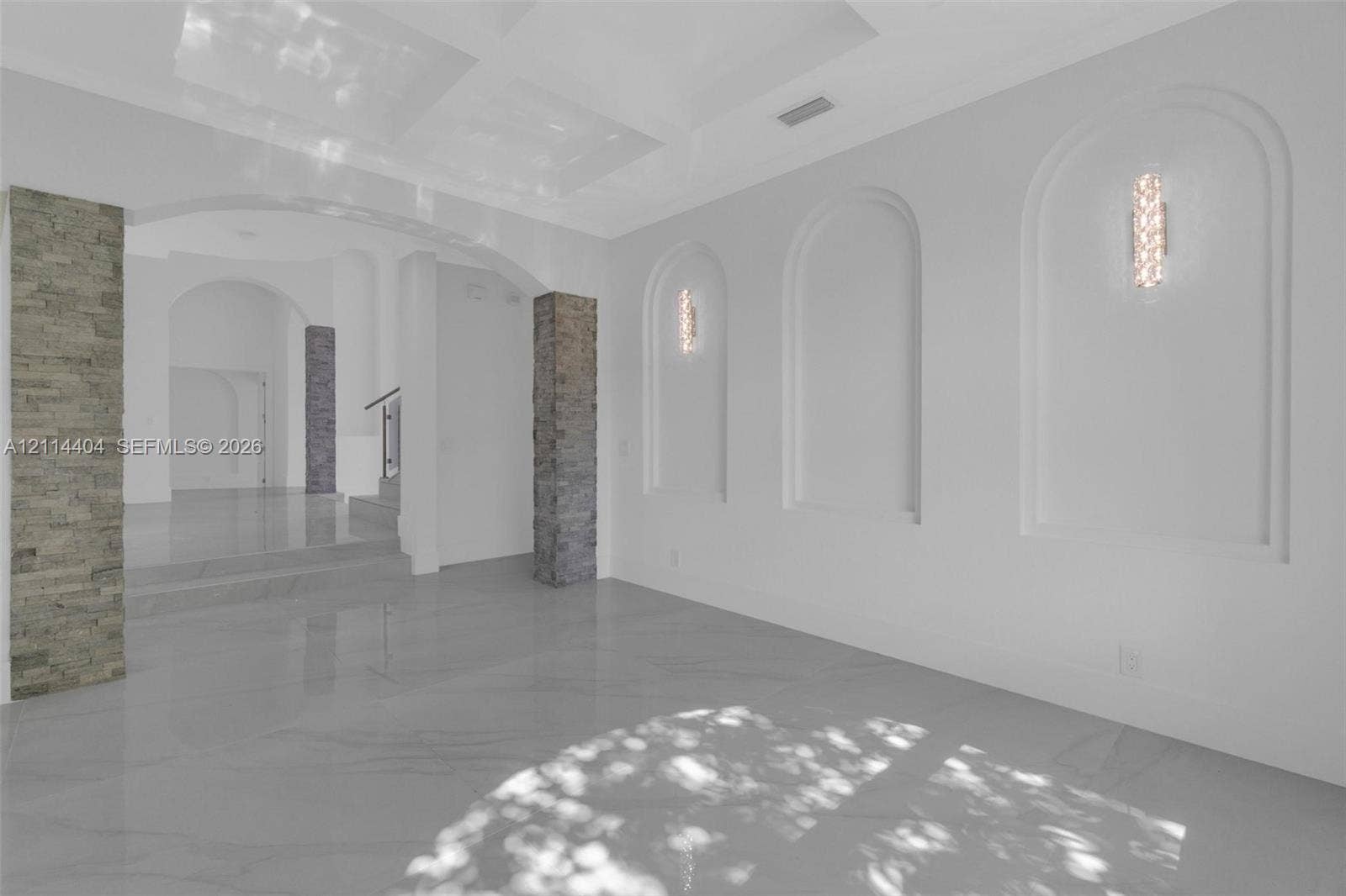 Large-format tile flooring, recessed wall niches, decorative stone-veneer columns, and wall-mounted light fixtures