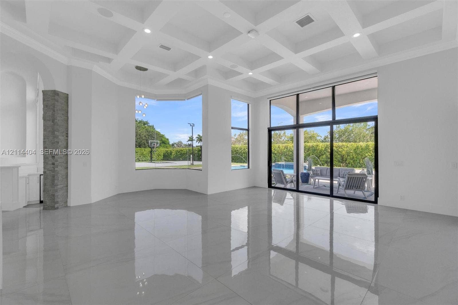 Coffered ceiling, polished stone-finish flooring, floor-to-ceiling windows, stacked stone pillar accents, and sliding glass wall system