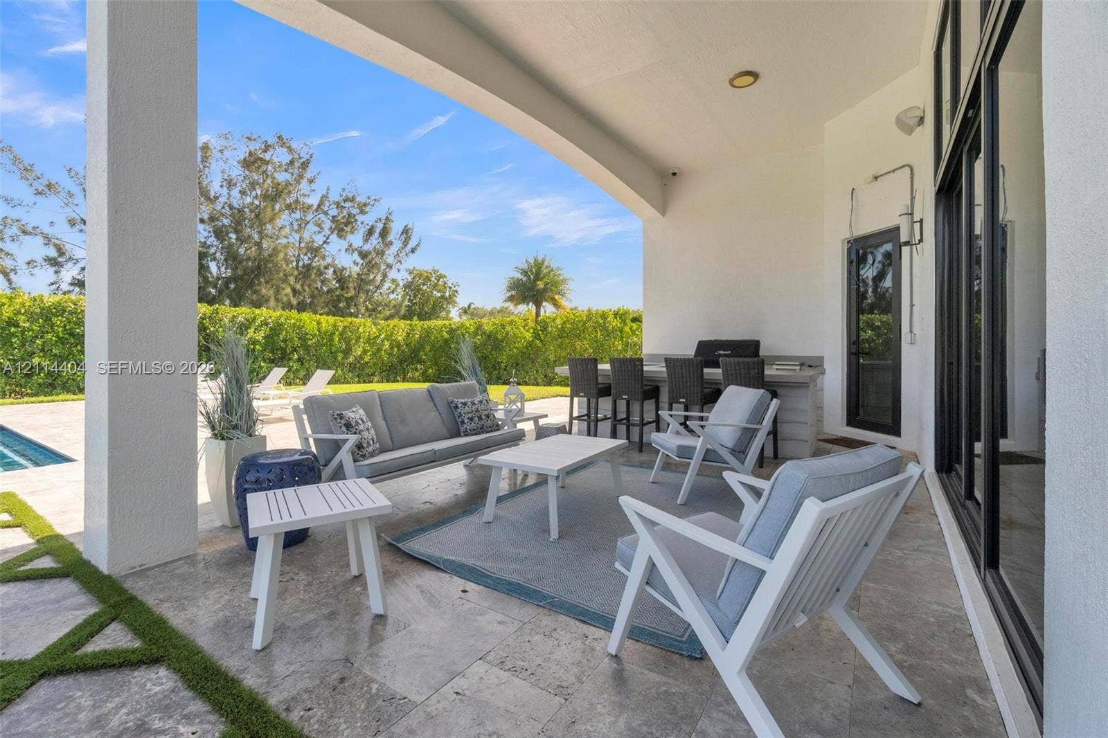 Covered patio featuring stone-tile flooring, a built-in outdoor kitchen with a bar counter, and expansive glass sliding doors