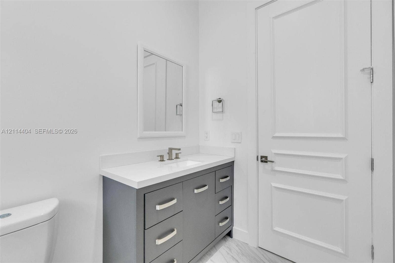 Grey vanity with stone countertop, rectangular undermount sink, widespread faucet, framed mirror, and multi-panel solid interior door