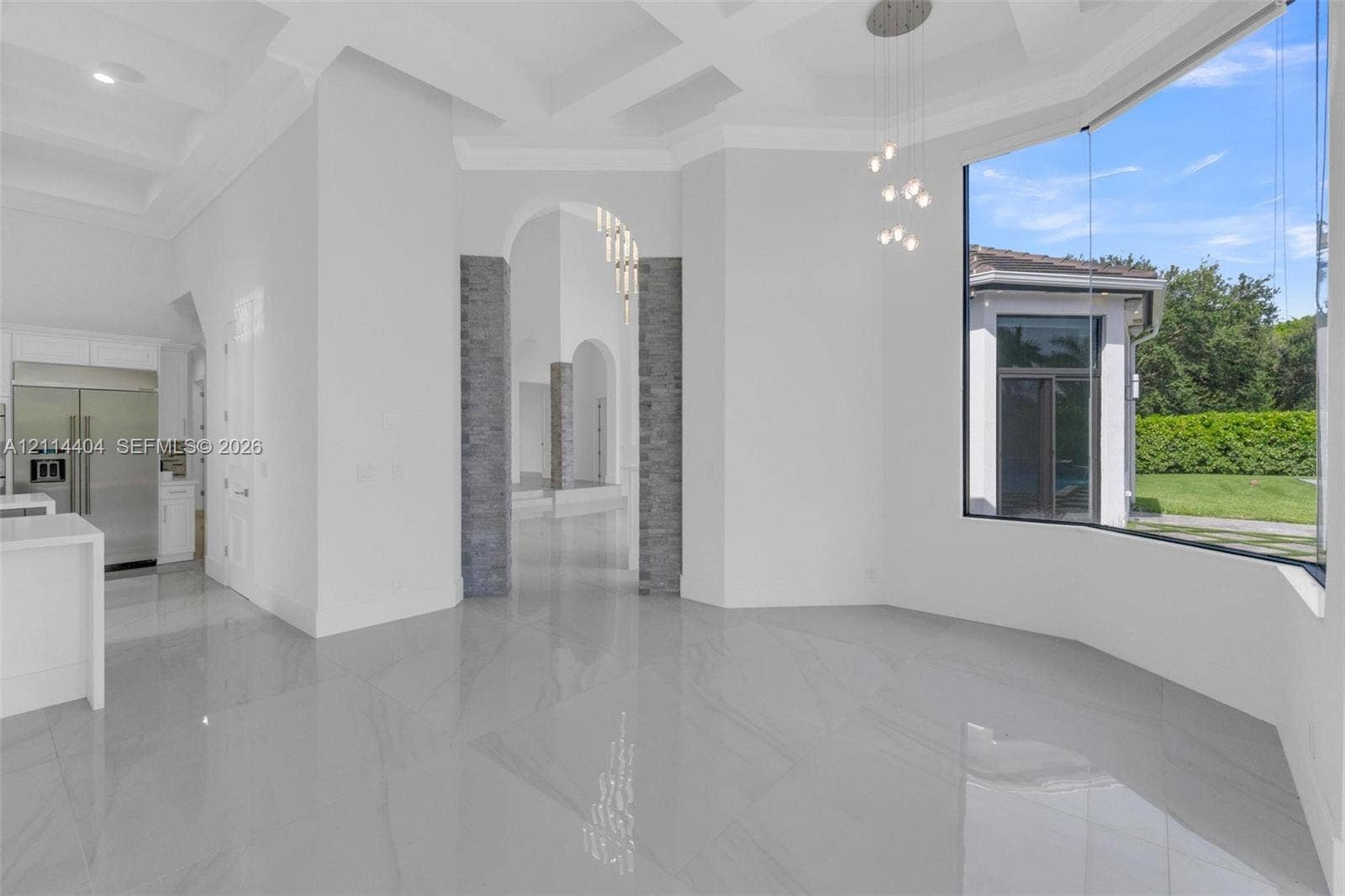 Coffered ceilings, large-format tile flooring, stone-clad arched entryways, and floor-to-ceiling windows featuring custom pendant lighting