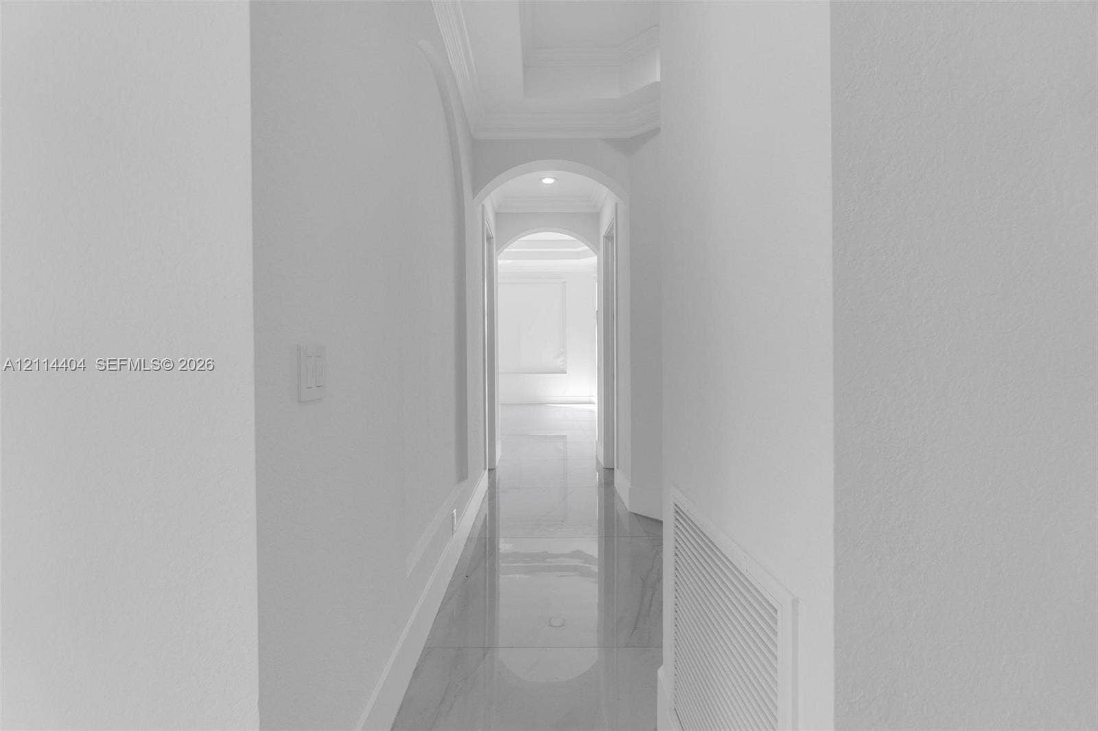 Hallway featuring arched architectural detailing, recessed ceiling lighting, and polished stone-finish flooring