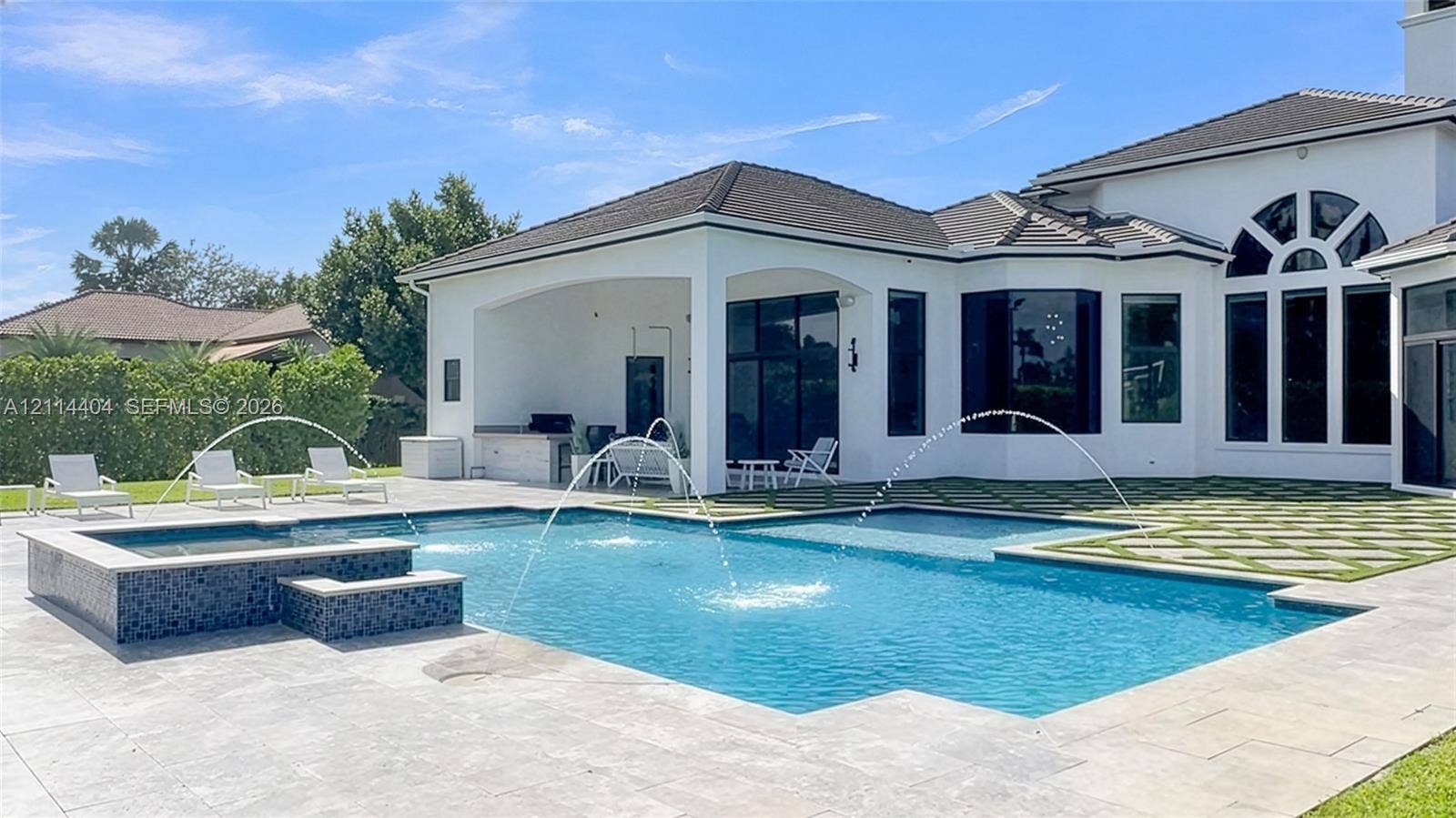 Swimming pool featuring built-in water fountains and a tiled spa, stone patio, covered outdoor area with a built-in grill station, and geometric paver accents