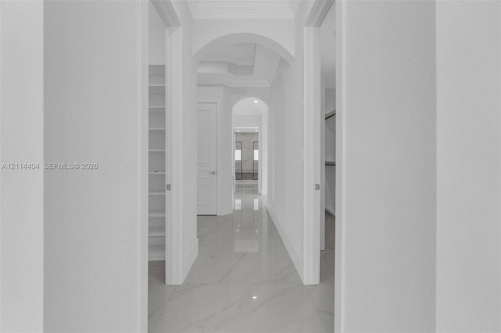 Hallway featuring porcelain tile flooring, architectural arched doorways, crown molding, and built-in shelving