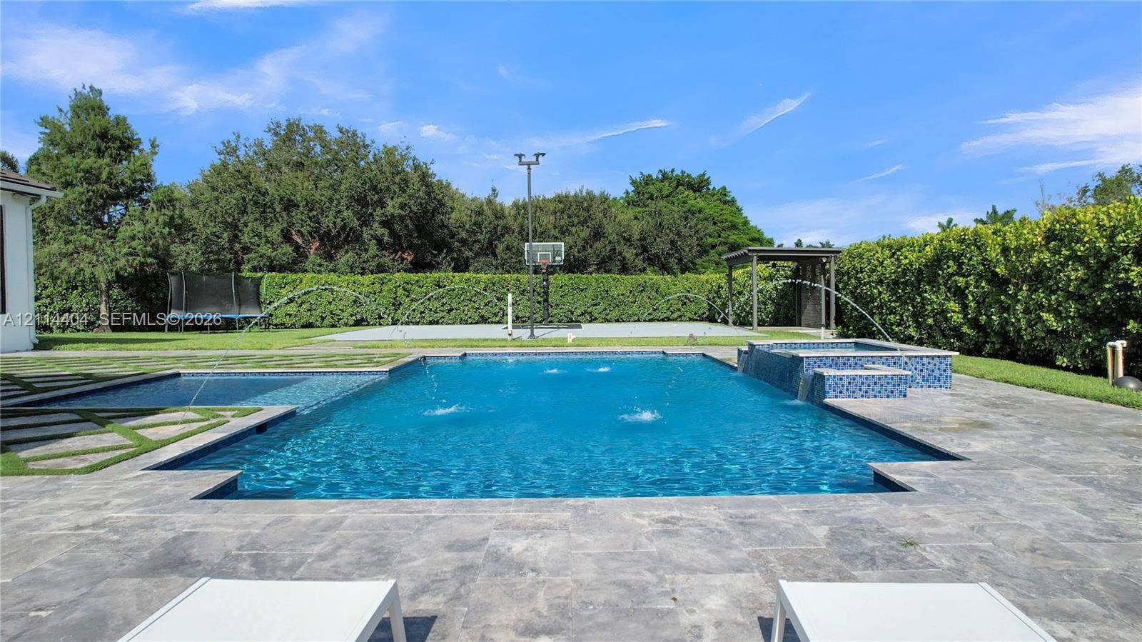 Backyard featuring an in-ground pool with water features, an attached spillover spa, stone-finish paver patio, and a concrete-surfaced sports court