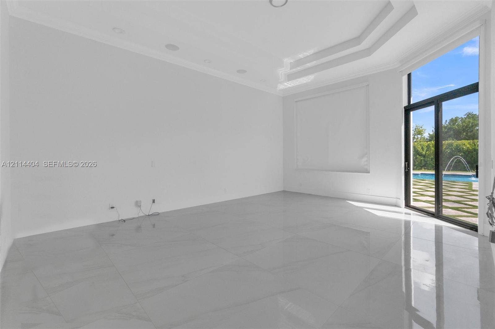 Interior space featuring large-format tile flooring, recessed ceiling lighting, a multi-tiered tray ceiling, and full-height glass sliding doors leading to a paved patio and pool area