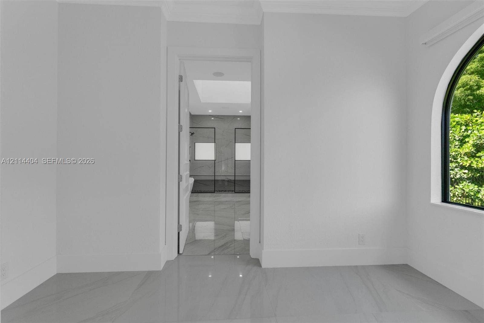 Large-format stone-finish flooring, arched window with black trim, and door opening to a space with recessed ceiling lighting and a skylight