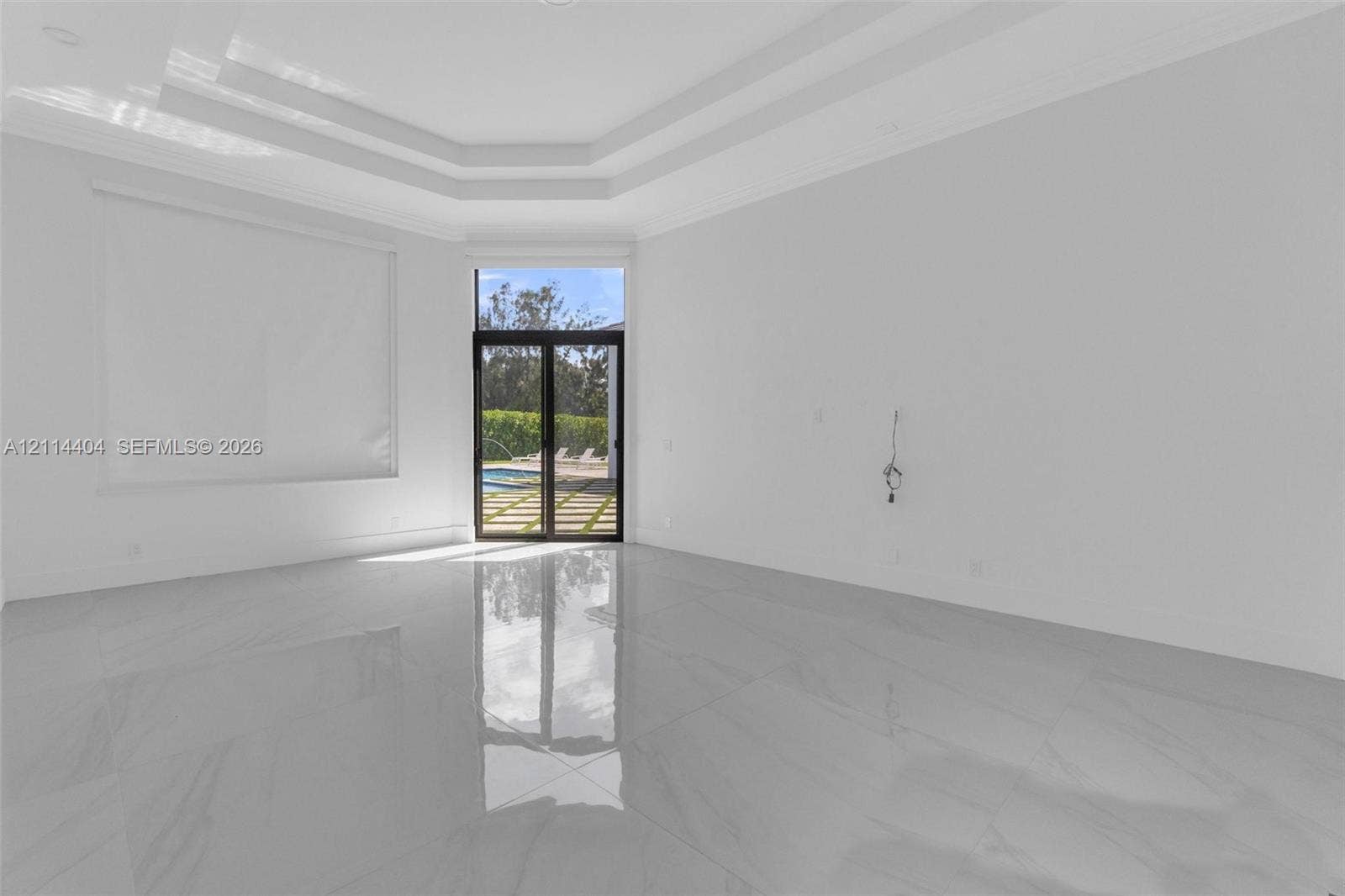 Expansive living area featuring polished large-format tile flooring, a multi-tiered tray ceiling, and sliding glass doors with dark frames providing exterior access