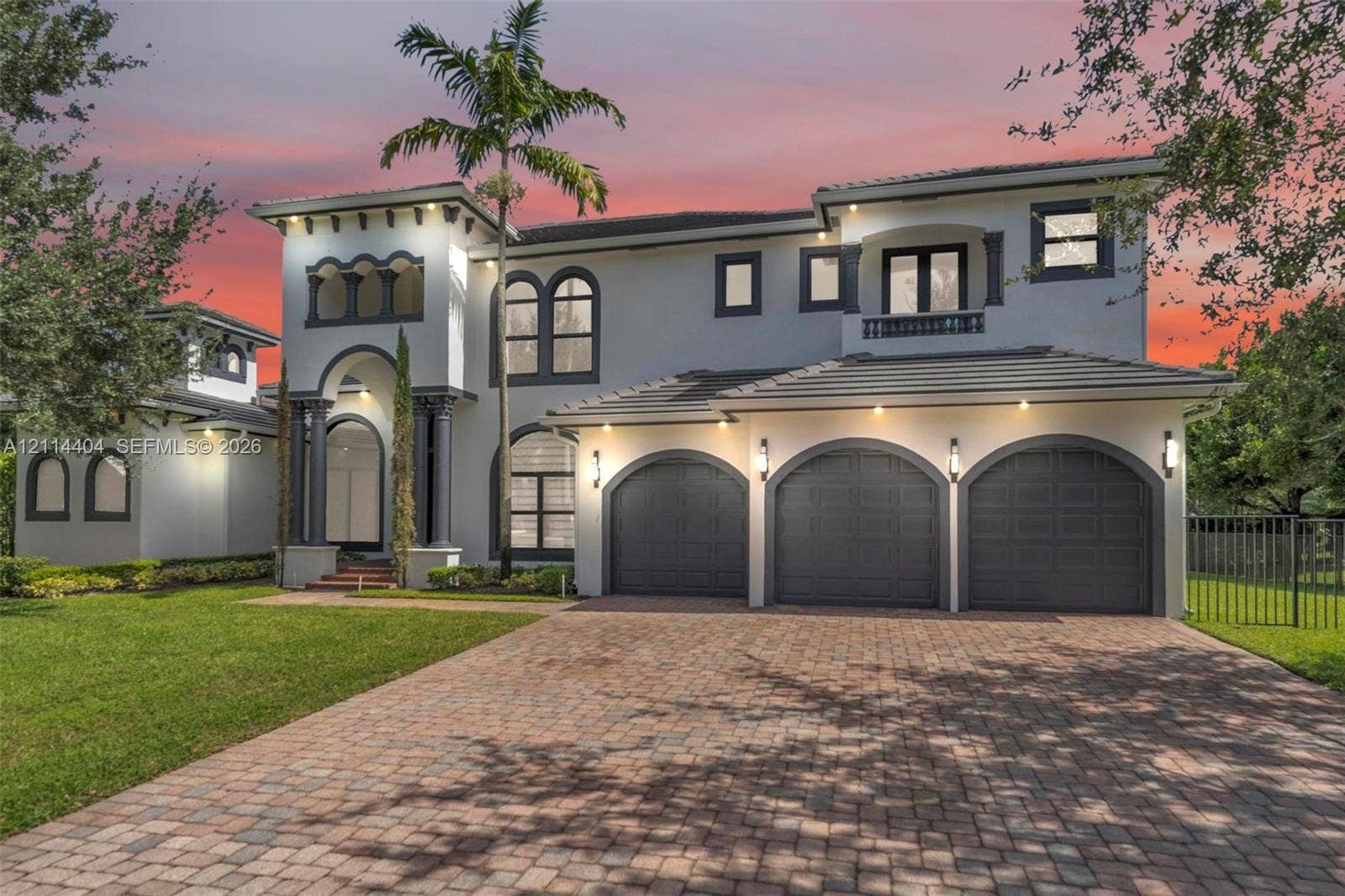 Two-story stucco exterior with arched detailing, concrete tile roof, paver driveway, and a three-car garage