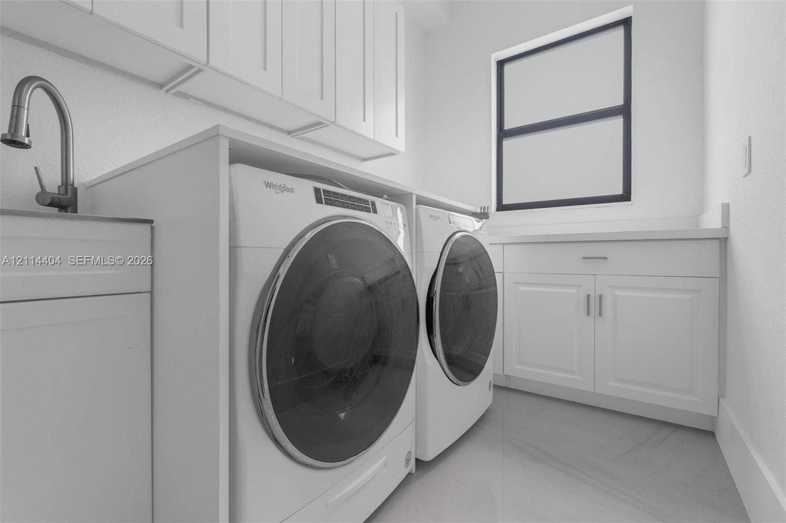 Laundry area featuring white shaker-style cabinetry, a built-in sink with a high-arch faucet, solid-surface countertops, and large-format tile flooring