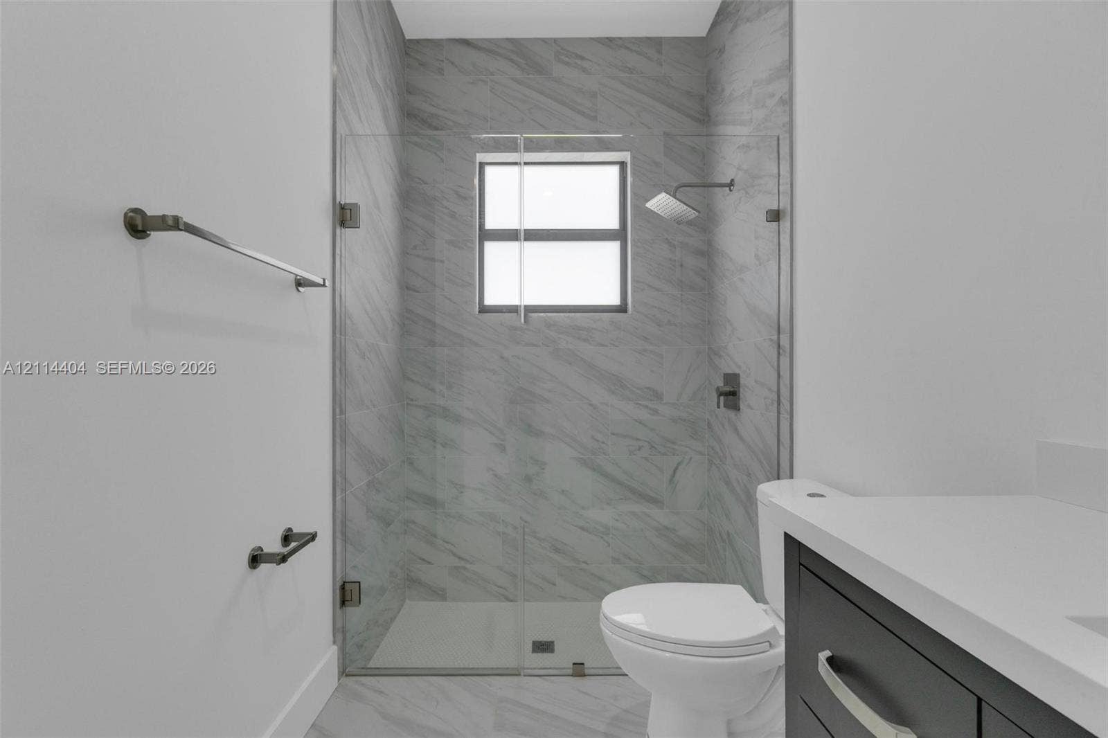 Walk-in shower with floor-to-ceiling neutral tile, frameless glass enclosure, dark-finish rainfall shower head, and dark-finish hardware