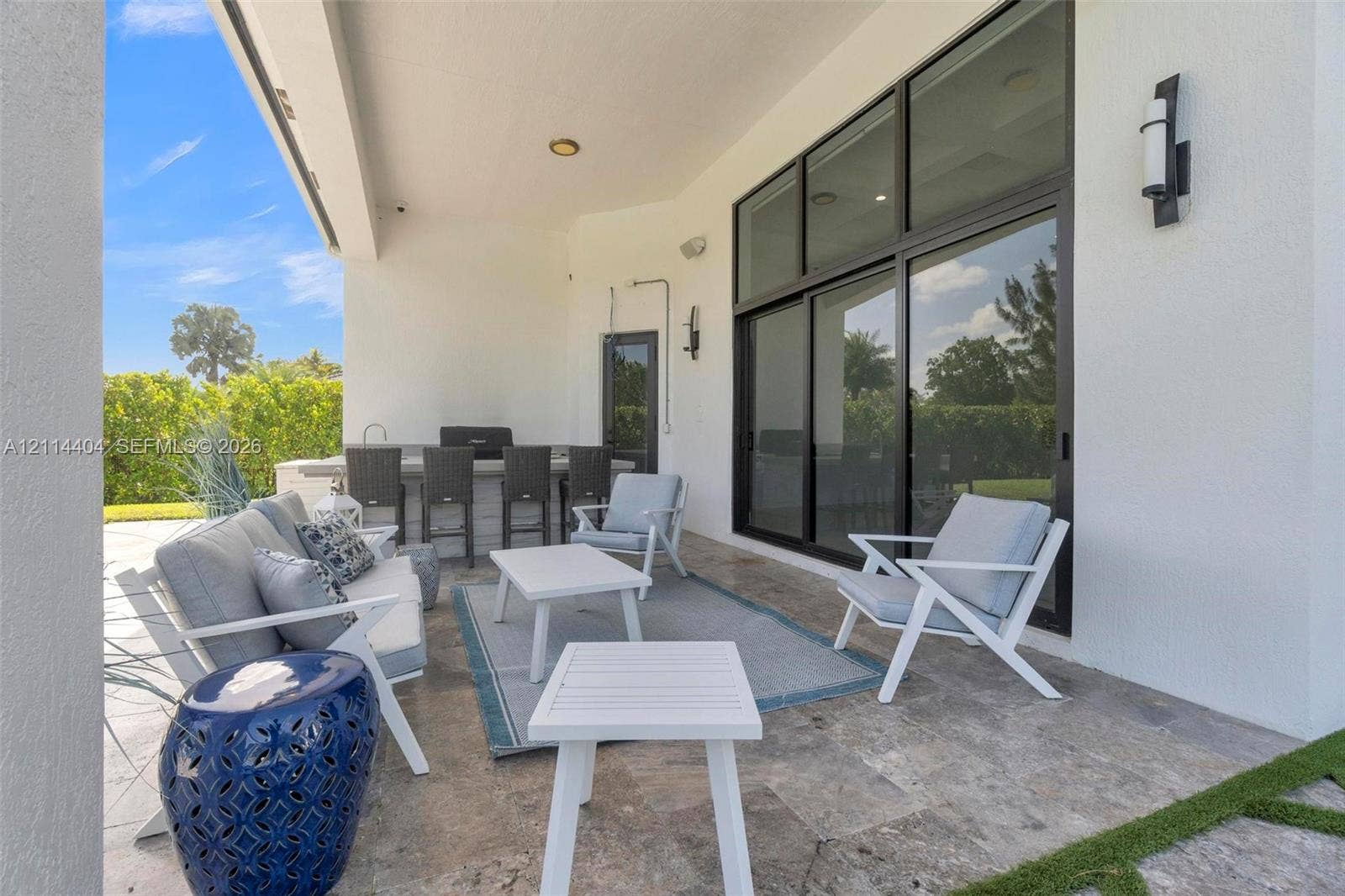 Covered outdoor patio featuring natural stone flooring, an integrated wet bar, and expansive sliding glass doors with dark frames