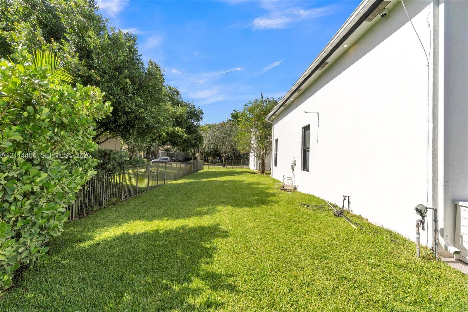 Side yard featuring a manicured lawn, perimeter metal fencing, and mature landscaping