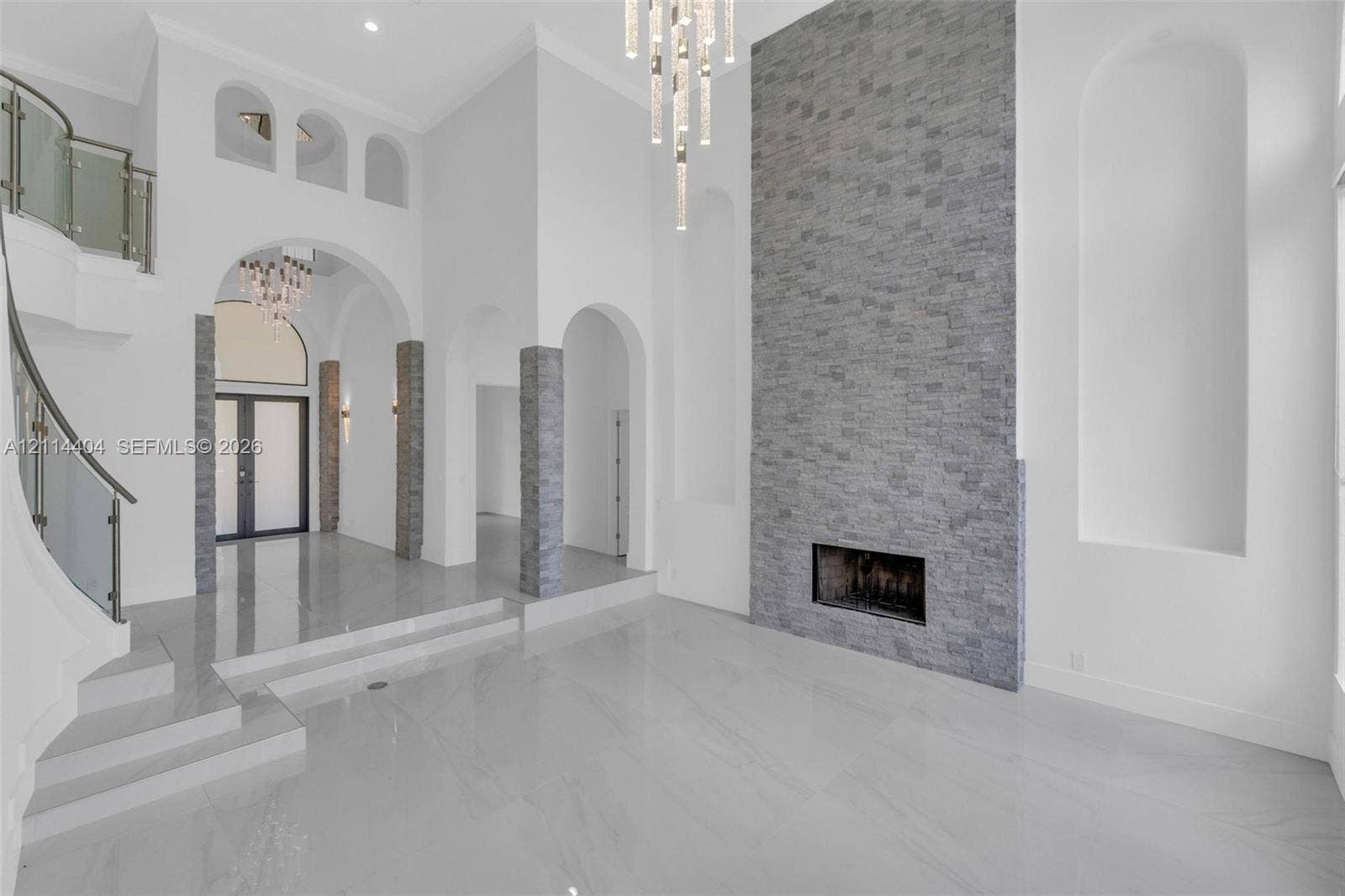 High-ceiling foyer with polished tile flooring, stone-veneer fireplace wall, architectural archways, built-in display niches, and a curved staircase featuring a metal and glass railing