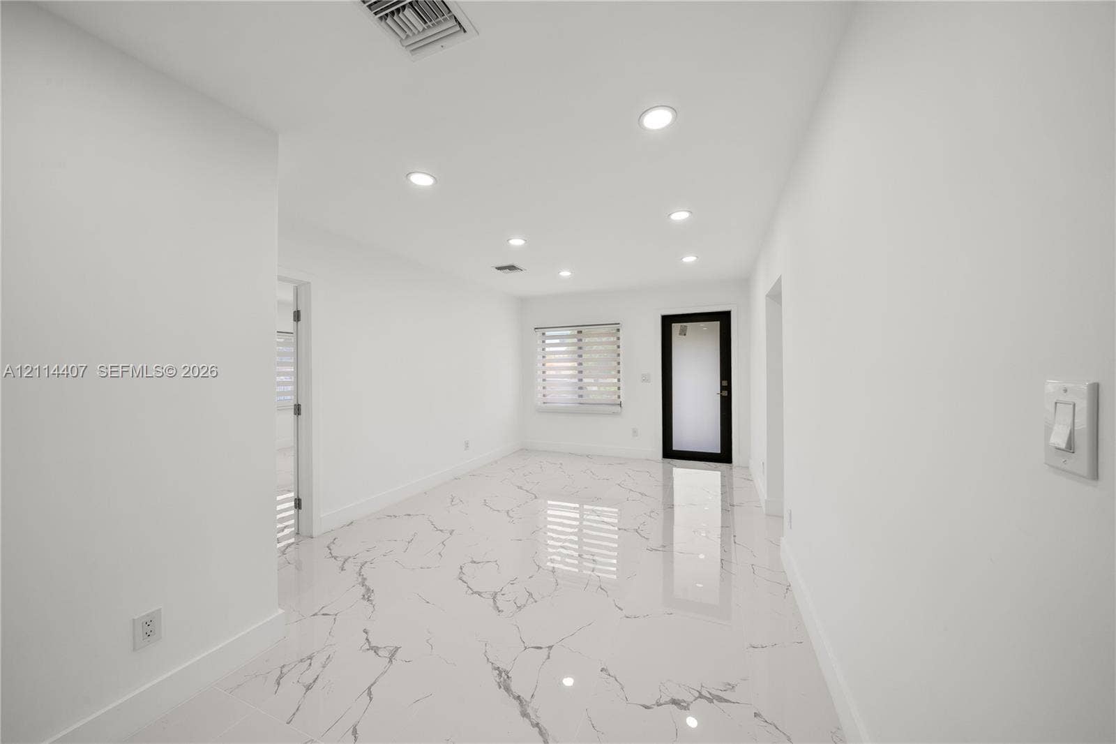 Polished stone-finish flooring with veining detail, recessed lighting, and an exterior door with a glass inlay