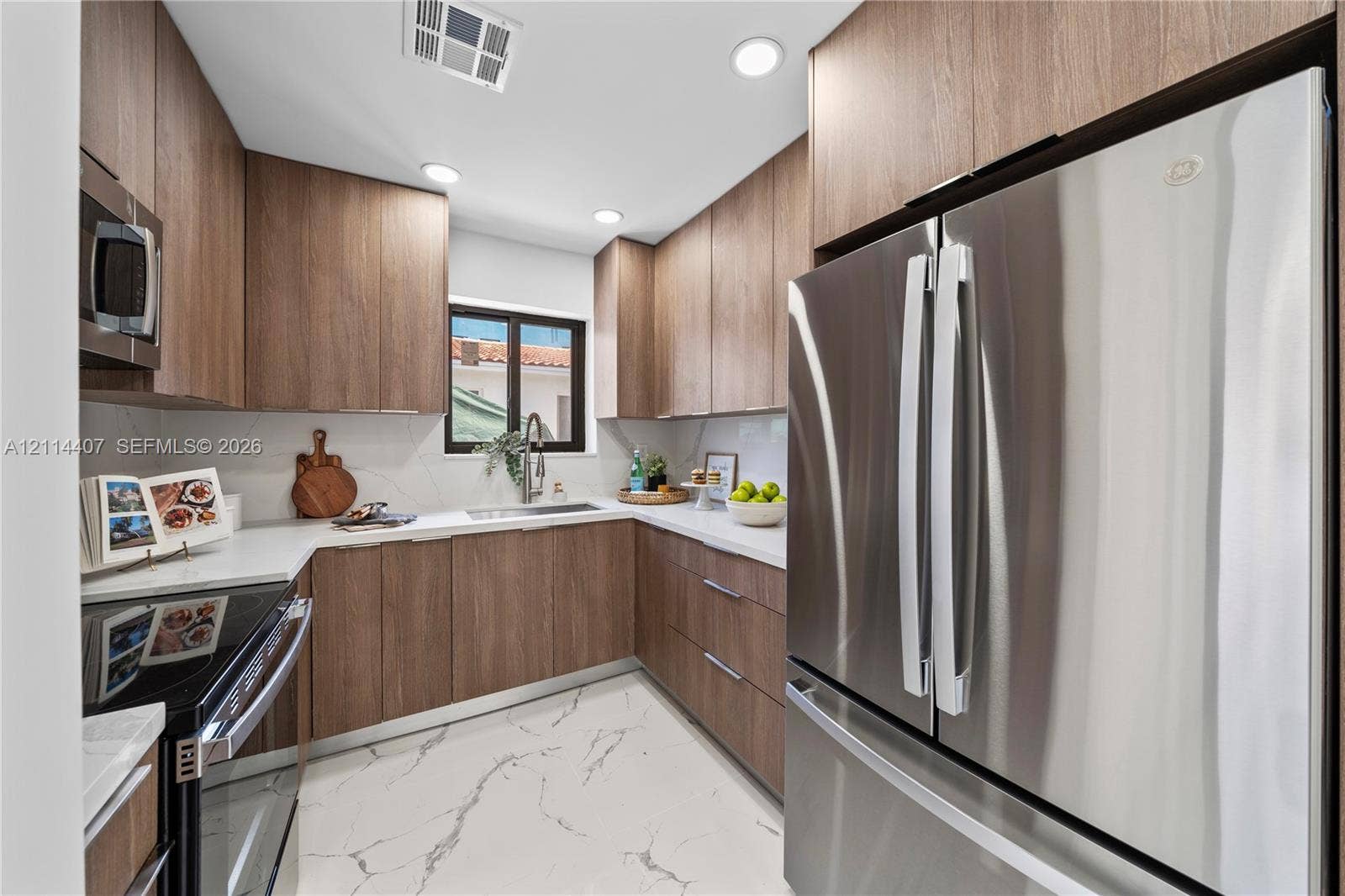 Kitchen featuring wood-finish cabinetry, white countertops, full-height stone-patterned backsplash, stainless steel appliances, and large-format tile flooring