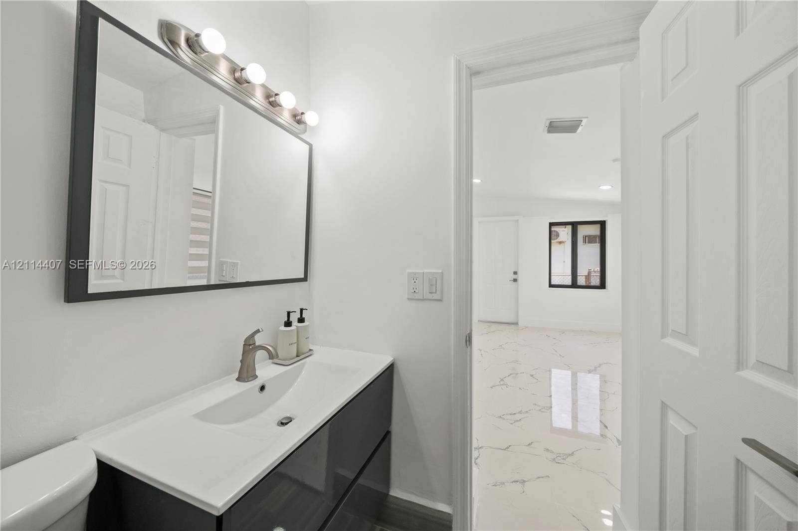Modern floating vanity with a white integrated basin, polished metal faucet, rectangular framed wall mirror, and vanity light fixture, featuring polished white tile flooring with dark veining