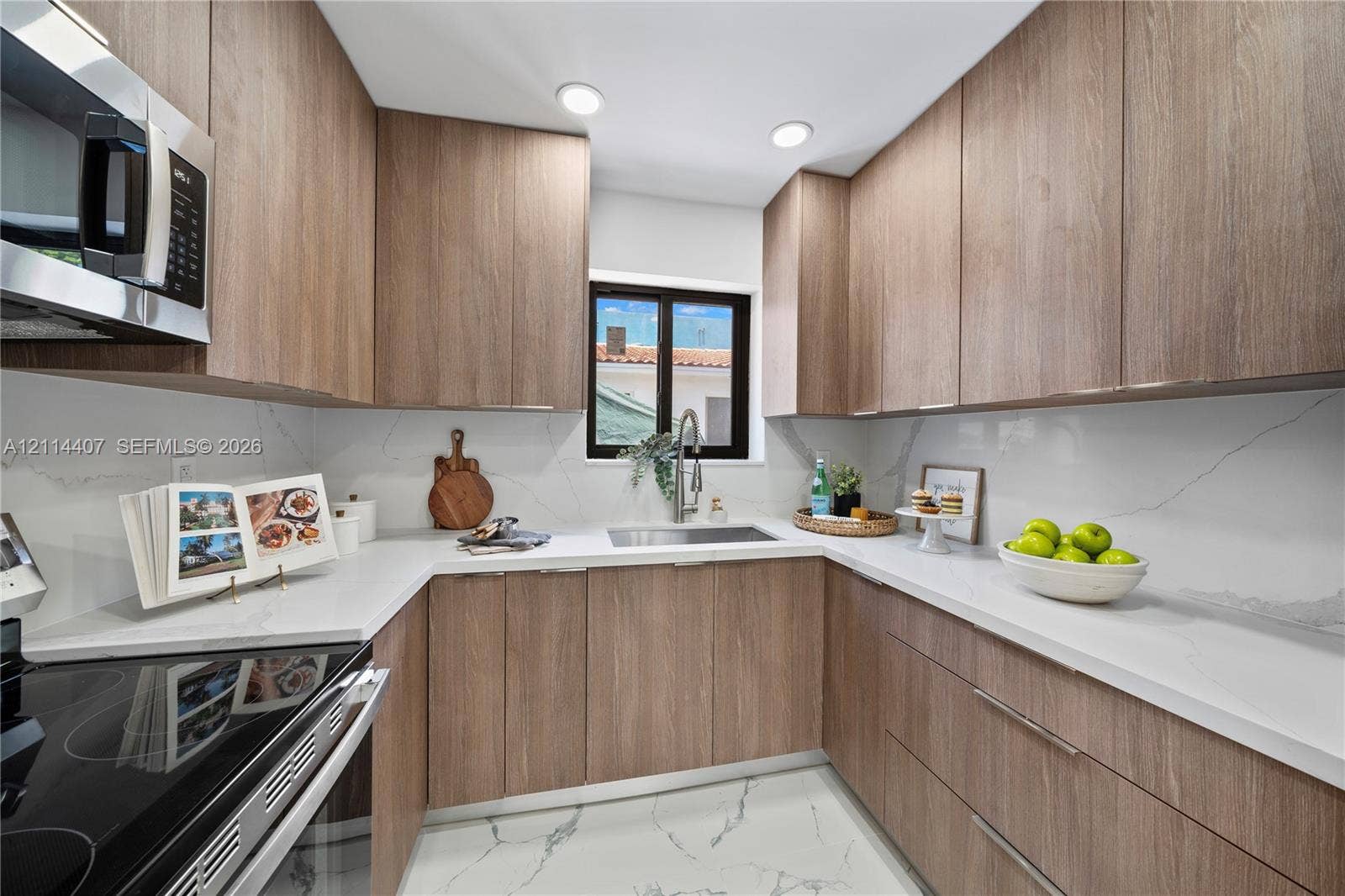 Kitchen featuring slab-style wood-finish cabinetry, white stone-surround countertops, full-height stone backsplash, undermount stainless steel sink with pull-down faucet, and integrated stainless steel appliances